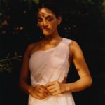 Rukmini Vijayakumar Instagram - “Once I enter the imaginative sphere, the world falls apart leaving the dewy grass, the moist leaves of the overhanging tree, the rays of sunlight escaping between the foliage of trees, and the silhouetted form of shiva in the distance to remain. I’m overwhelmed as he moves to adjust his matted locks over his shoulder… his sharp nose etched into the skyline behind. I can’t take my eyes off of him…. He looks my way and I turn away… am I shy? “ Photo @suleikamueller Styling @aartthie Featured in @vogueindia #parvati #shiva #srishti #imagination #performer #bharatanatyam #shivapurana #indiantradition
