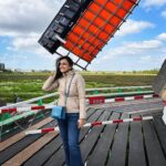 Niyati Joshi Instagram - Cold and crazy wind makes you forget FASHION 😂 It's all about SURVIVING the blustery wind. That's a windmill fan blade in the background in a Dutch country side village called ZAANSE SCHANS ,famous for its wooden windmills . #zaanseschans #amsterdam #europe #countryside #actor #niyatijoshi Zaanse Schans- A Windmill Village