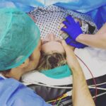 Ali Bastian Instagram - It’s #csectionawarenessmonth I thought I would share my story again. The moment that changed my life forever ❤️ *We managed to get some incredible photos of Isla’s birth, courtesy of the operating theatre staff but this is one of my absolute favourites. This was moments before she was born. David is right by my side supporting me as always, but what I didn’t anticipate was that I would also have a right hand woman. Those blue gloved hands that are holding mine belong to her. Georgie, my anaesthetist. I was blown away by the kindness I experienced from all of the doctors, nurses and consultants... but this beautiful soul sticks firmly in my mind. As well as monitoring every aspect of my physical health and wellbeing, she somehow had the capacity to support me emotionally and mentally, talking me through every aspect of what was happening... Excitedly letting me know when it was nearly time to meet my baby and most memorably... holding my hand when I was scared. I was such a heady mix of excitement and anticipation... but also more nervous than I think I had ever been about anything. I had never experienced such a large medical procedure and when I arrived in the theatre, my teeth were chattering with adrenaline! My blood pressure dropped a couple of time during the op and she calmly and proficiently adjusted my sails and then held my hand to steady me. She made me laugh with her dry, razor sharp wit and showed me kindness and compassion when I cried and was overwhelmed with emotion. Thank you Georgie, I will never forget you. I’m so grateful to you and everyone at @chelwestft ... there are so many people that left such a lasting impression on me, I will definitely tell you about some of the others. I think about them all the time and pray they are keeping safe and well Xxxxx *