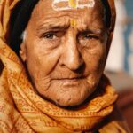 Arjun Kamath Instagram - In the quiet embrace of dawn, at the venerable Nepali Mandir in Varanasi, a voiceless testament of faith unfurls. An elderly dame, her face the chronicle of years, still radiant under a golden glow of sunlight. Etched lines, tales of time, seem to converse with the divine, further illuminated by those enchanting, expressive brown eyes. She's draped in a holy saffron scarf, a spiritual armour against worldly follies. A prayer whispered, she turns towards my lens, a moment frozen in time, her aura echoing amidst the slowly stirring symphony of Varanasi. In her silence, a thousand stories sing. Her gaze, the pulsating heart of this city. A portrait capturing not just a woman, but an essence of an ageless India. #CapturedOnCanon with a @canonindia_official EOS R5 #arjunkamathphotography #photography #portrait #portraitmood #portraitpage #woman #old #eyes #naturallight #sunrise #holy #prayer #temple #streetphotography #travelphotography #varanasi #banaras #india #incredibleindia #DoGreatWithCanon #MentorsInFocus #EOSMaestro #instagood #instamood #instagram #instaphoto Varanasi, India