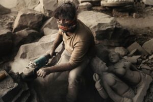 Arjun Kamath Instagram - The evening light was growing golden by the minute when I was driving through the quaint city of Khuldabad in Maharashtra. On the way, I saw an unusual whirlpool of dust outside my car window, so I decided to stop. As I cut through the flying dust, I saw a man engrossed in sculpting, his hands masterly guiding the machine that fervently chipped at a stone slab. 

Having acknowledged my presence, he carried on with the arduous task in all sincerity. I took the time to walk around and explore his petite workshop, which was decorated with half-made figurines and fine sculptures. The dusty haze of grey all around with the only colour being that of the man’s vibrant mask stood out for me, while the figurines in the background hinted at his work of the past few days. Intrigued by the whole setting, I quietly took the hold of my camera. In that exact moment, he looked up for the very first time and that was a sign enough for me to click on the shutter button of my camera.

It was only later when we got talking that I could know more about him. His name was Hiralal Chauhan, and along with his family, he spent most of his time sculpting figurines out of kala patthar. Other talks were shared, about his work and how he has pursued it for 20 years. But the thing that stayed the most with me were his parting words. He told me that he was not able to pay due attention to me because his work demanded precise attention and a distraction of even a split second could result in grave injury. As he uttered those words, I was taken aback and could only see him in a light of greater respect.

I believe that is what I love the most about travelling, that it allows me to learn more about the world and the people who live in it. Through my frames, I try to capture a sneak peek into people’s lives and tell their stories, capturing the essence of their personality. In a way, this act makes all my travels creatively fulfilling and fruitful, and I see it as one of the most enjoyable things about photography. 

 
#CapturedOnCanon with a Canon EOS 5D Mark IV & a 24-70mm F/2.8 II Lens

#arjunkamathphotography #portrait #man #carving #stone #khultabad #aurangabad  #yourshotphotographer