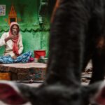 Arjun Kamath Instagram – This is a city where peace and chaos meet.
Where ashes rise, and virtues breathe.
Her streets are coloured with stories untold,
Some sights to ponder and some to behold.
And no matter how inward you go, how deep you dive.
You’ll forever find treasure but never arrive.

Varanasi, to me, is a city that never ends. It is as if the city’s stories, people, events, and mysteries have been playing an ages-old game of tag– always being passed on but never coming to an end. 

On my recent visit, I had the chance to rise early on with the city and make myself a part of its humdrum. On a dewy Wednesday morning, I awoke at 4:30 in the morning, looking forward to the soothing boat ride from Dasashwamedha to Assi Ghat. A serenading hour in the boat and a blissful arati later, I found myself in the winding gullies just close to the Manikarnika Ghat.

With a choice of a new path after every dozen steps, Varanasi unfolds slowly and amusingly in these serpentine streets. I admired the soft light that painted the morning tender with a left turn here and a right turn there. The locals chattered away about their mohallas and the affairs of the city, pausing every once in a while to relish the ring of a temple bell somewhere. An ever-changing cluster of cows, street dogs, and fragile-looking two-wheelers kept me company as I walked without a motive, simply taking in the distinct way of life that Benaras is known for.

At one of these many turns, I came across this gentleman sitting on a tiny stone porch, sipping his morning tea without a care for the world. In the chaos of the city’s everyday events, he seemed to have built his own pocket of peace. And at this sight, I couldn’t help but admire the character on his face and the textures and colours that enveloped him.

As I took hold of my camera to take a picture of him, an unbeknownst cow happened to walk right into the frame, as if quietly claiming her presence. Smiling, I thought how perfectly this captured the raw and free-spirited essence of Varanasi and clicked the shutter button on my camera.

#CapturedOnCanon with a @canonindia_official EOS R5 with a RF 24-70mm F2.8 Lens

#arjunkamathphotography #varanasi #portrait #india Varanasi, India