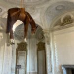 Daniela Collu Instagram - C’è un cavallo imbalsamato appeso in mezzo alla stanza di un museo: è un’opera di Maurizio Cattelan e si intitola Novecento. Ne ho visti un milione di cavalli nei musei, ritratti in posizione rampante, solenni nelle sculture equestri, dipinti nei paesaggi ottocenteschi, morenti nelle scene di guerra di tutte le epoche, a terra, galoppanti, in mandrie, solitari, ma così mai. Il collo è deformato, allungato dalla gravità e dalla tassidermia, le zampe a guardarle da sotto sembrano più tozze, più lunghe e larghe, e un senso di precarietà pervade i sensi, mentre si attraversa la stanza sotto questo peso galleggiante, immobile, inerme. Si chiama come il secolo in cui siamo nati, quello in cui la maggior parte delle sciagure che ora non sappiamo manovrare sono state costruite, un secolo di errori, di scoperte, di sconfitte e vittorie, di grandi passi per l’umanità e di crisi esistenziali senza ritorno. È la natura morta più disorientante, straniante e cruda che si possa immaginare, parla di simboli decaduti, di corpi infranti, di certezze mancate, di fallimenti annunciati. Di quel senso di impotenza e di inerzia umana che ancora, in un nuovo secolo, ci soffoca terribilmente. #unminutodarte Castello di Rivoli Museo d'Arte Contemporanea