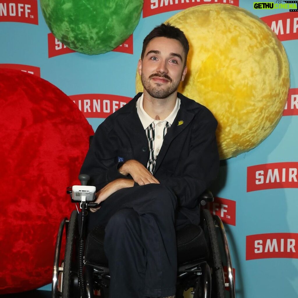 George Robinson Instagram - #ad I had a great time celebrating the launch of @smirnoffeurope WE DO US Live. While I love a good party, it’s way better when everyone can be a part of it. That’s why making nightlife more accessible is so important. @smirnoffeurope and Disability-led organization @tiltingthelens are working together to improve accessibility by supporting the Disabled community in clubs, bars and pubs - more to come! To everyone involved - thank you for such a fabulous night and showing easily it can be done. ************ Image Description: George Robinson is a white, masc wheelchair user. He has green eyes, cropped, dark hair, a moustache and dark stubble along his jawline. He is wearing a dark jacket and chinos and a white and black houndstooth polo shirt. He is wearing thick, textured brown socks and black leather shoes. On his lapel he has a small light green pin. He is positioned in front of a sky blue branding board, with the red and white Smirnoff logo repeated all over and red, green and yellow spheres covered in felt as a decoration. He is smiling for the picture and is at the Smirnoff ‘We Do Us Live’ event, celebrating accessibility in music. The event took place on 29/11 at 26 Leake Street in London.