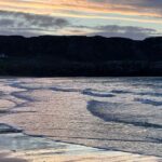 Louise Brealey Instagram – We drove west along the north coast of Scotland into the dazzle of a sunset and made it to the beach just before the sun slipped down behind a band of cloud.
There was a smushed marigold on the tide line. I walked the quarter mile to our bit of the beach, where a scree of giant pebbles meet the sand. On my phone is a picture of mum sat here with a towel on her head.
I put the marigold on the rocks. The Mexicans call it the flower of the dead and use its bright colours to guide the spirits of their lost ones to their shrines on the Dio de los Muertos.
I ran my fingers through the fine white sand and let the sea and the sky do their thing.