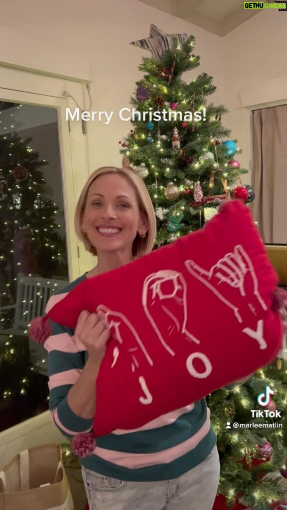 Marlee Matlin Instagram - #merrychristmas #asl #signlanguage #happyholidays Image description : Marlee Matlin signs “Merry Christmas” in American Sign Language, then pulls out a red pillow with the word JOY spelled out in ASL