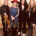 Pam Tillis Instagram – Behind the smiles….. words can’t even express how hard it is to watch all that’s happening on the world stage today. 
The gentlemen next to me is a fantastic guitarist and singer from Romania that happens to be playing with us… Alex Kilroy. His mom is a nurse at a hospital 200 miles from the Ukrainian border. All of my group.. Haley, Carson, Terry,
We know how fortunate we are to be playing music and trying soothe nerves and help people forgot for a moment how scary it all seems. So grateful. Even as we play my home state of Florida a world away our hearts are very much with the people of Ukraine who are suffering, those who are working for, fighting, and praying for peace. And also the brave Russians protesting and the other countries where people are taking to the streets with a message of love and not destruction. That’s all I got for now…….. this is just starting and I’m already emotionally spent.