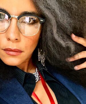 Parisa Fitz-Henley Instagram - Why choose one? Trent Crimm: The Independent Woman Jackie Collins. Happy Halloween, yall! 🎃😈🤓

Image Description: 
1. Me with big gray-streaked frizzy hair, Trent Crimm glasses, Jackie Collins makeup, gray jacket and black button-down either of them could wear, silver dangling earrings, red lanyard that reads “Independent”, a notebook and pen. 
2. Trent Crimm (of The Independen and Ted Lasso fame) in glasses, blazer, button down and tie. His face framed by luscious gray hair. 
3. Jackie Collins, novelist extraordinaire, big frizzy delicious 80’s hair, loads of dramatic 80’s makeup, leopard print blazer/choker/earrings, staring down the camera like she’s about to pounce. 
4. Me continuing to feel myself but this time with a bit of a pearl and diamond(ish) choker peeking out at my neckline)