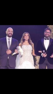 Tamer Hosny Instagram - لكل اللي بيسأل عن ايه وجه القرابه بيني و بين العروسه الجميله دي شايف اسأله كتير انا هحكيلكوا 😀هي اسمها هاله عمر عرفتها كانت بنت من الفانز صغيره و من المقاتلين و المدافعين عن تامر على الانترنت 😀💪و من كتر دفاعها عني لفتت نظري و مره رديت عليها شكرتها و لما سافرت اسكندريه في الوقت ده لقيت بنت صغيره اوي بتعيط و بتجري عليا فا وقفتلها و فكرتني بنفسها و فضلت تعيط 😢و تقولي احنا معاك و لازم تكمل عشان كنت بتحارب جداً في بداياتي فا اتصدمت ان اللي بتقول كده بنت صغيره كده و المجهود ده كله اللي عاملاه بنت صغيره عندها ١٤ سنه وقتها كانت السوشيال ميديا لسه بتطلع و كنا في شركتنا بندور على شركه كبيره تمسكلي السوشيال ميديا لحد ما قولتلهم انا مش عايز شركه كبيره انا عايز البنت الصغيره دي هي اللي تمسكها فضلوا يقنعوني ان كده مش صح ولازم اكتر حد خبره يمسكها وانا قولت لا لازم اكتر حد بيحبني هو اللي يمسكها و انا واثق ان طاقة الحب مفعولها اقوى من طاقة المحترف بلا حب فعرضت عليها تشتغل معايا و هي في السن ده مصدقتش طبعاً و من ساعتها و هي اللي ماسكه كل شغل الميديا الطفله الشاطره اللي كبرت دلوقتي قدامكم هاله عمر ،،، اما بقى عريسها العسل ده اسمه عمرو طلب اديها مني انا عشان والدها و والدتها توفاهم الله. في سنه واحده رحمهم الله ياريت نفتكرهم و نهديلهم ثواب الدعاء و الفاتحه .. و من اللحظه دي اتحولت هاله لبنتي الكبيره بجد اللي بتتجوز دلوقتي قدامي و بسلمها لعريسها بنفسي و بغني في فرحها ، معرفتش ارد على كلامك عني في الفرح يا هاله رديت دلوقتي هنا ربنا يكرمك و يسعدك مع جوزك الجميل المحترم اللي هيكون ضهرك و سندك و يكمل معاكي مشوار حياتك مع اولادكم الجُمال بإذن الله 🤲 @halllaomar @amrserag1 @ahmedyassinweddingplanner @tareksabry1 @menam_photography