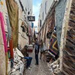 Vera Kolodzig Instagram - Dia 13: Conhecida como a “Cidade Ventosa de África”, Essaouira atrai muitos kitesurfers durante o ano inteiro, no entanto há muito mais do que o areal a perder de vista, ou o cenário do Game of Thrones. O sultão Mohammed Ben Abdallah instalou-se aqui no século XVIII e contratou um arquitecto francês para desenhar uma cidade no meio do vento e da areia onde nada existia antes. Originalmente chamada de Mogador, o sultão mudou o nome para Essaouira que significa “bem desenhado”, com a sua mistura única de estilo marroquino e europeu. Chegámos ontem à noite, já com mesa marcada num restaurante sugerido por um amigo, onde reencontrámos a amiga que fizemos em Tarifa na noite antes de iniciarmos a viagem. Acabámos num nightclub onde uma troca de olhares nos levou a conhecer os melhores guias que podíamos desejar. A manhã de hoje foi na praia, com um mergulho salgado para lavar a alma. Surgiu então a possibilidade de ir à lota comprar o marisco mais fresco que alguma vez vi. Ao passar o arco do kasbah parecia todo um novo mundo, com as embarcações já atracadas e dezenas de pessoas a vender o que pescaram de manhã, enquanto as crianças se atiravam dos muros da fortaleza para o mar. Foi neste momento que decidi que se há locais para abrir excepções à minha habitual dieta, este é um deles, ainda assim mantendo os meus princípios - saúde e sustentabilidade. Duas lagostas, um caranguejo, camarões e uma conserva caseira, por 500dhr negociados pelos nossos amigos marroquinos. Depois levaram-nos pelo labirinto da medina até um terraço onde apenas famílias locais se deliciavam. Entregámos as nossas compras, e uma hora depois tínhamos uma mesa repleta das mais incríveis iguarias, por mais 60dhr - o custo do “aluguer” de um espacinho na grelha. Uma experiência que ficará para sempre nas nossas memórias e nos nossos corações, já com uma pequena nostalgia de uma despedida para breve. Amanhã começamos a subir, de barriga cheia e inshallah sem caganeira! . . . #roadtrip #morocco #essaouira #localexperience #instatravel #seafood Essaouira - Mogador - الصويرة