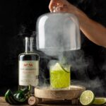 Bryan Cranston Instagram – It’s nearly the weekend, right? I like a bit of spice with my @doshombres margarita. Let me know if you’re brave enough to try… 

DH Margarita
1.5oz. Dos Hombres Mezcal
3/4oz. Agave Syrup
3/4oz. Lime Juice
3/4oz. Roasted Poblano Puree 
Pinch of Salt

Add all ingredients to a shaker tin filled with ice, shake vigorously, double strain over ice in a rocks glass. Garnish with a lime wheel and *optional smoked rosemary sprig.

*Roasted Poblano Puree: High flame on gas stove. Add poblano directly over flame, allow skin to bubble and blacken (2-3 min on each side), flip every few minutes, DO NOT allow to catch fire or turn to white ash, remove charred poblano and place in a small ice bath to cool, remove skin and discard, cut to remove stem, seeds and ribs; add to food processor, pulse until smooth. 

*Smoked Rosemary: Carefully smoke the end of rosemary sprig with a kitchen torch and blow out after a few seconds for extra essence.