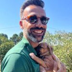 David Cristina Instagram - Apresento-vos a Sheila Marina, a cadela mais fofinha do mundo que agora vive cá em casa. Tudo começou com um grave erro. E o erro foi deixar-me convencer por uma veterinária amiga (da onça) a ir visitar a bicha. Gente, não vão. Não vão, porque é uma armadilha de fofinhice. Estes veterinários manipuladores sabem que quando olhamos para os olhos desta bicheza já não os conseguimos deixar lá. É o canto das sereias, mas em vez de afundar o barco, deixa um tarolo no tapete da sala. E pegadas de trampa pela casa toda, como se fosse a fábula do Hansel e Merdel. Para quem quer saber a etnia da Sheila (seus racistas) é um Cruzado Português, que é uma maneira betalhufa de dizer "rafeira". Não a comprei, atenção, salvei-a. Quando encontrei a bicha, coitada, deu-me tanta pena, estava ela para ali desgraçada, na Margem Sul. Já lhe estavam pintar as unhas e a fazer extensões quando agarrei nela e fugi. Em honra das suas origens, ficou Sheila Marina, para honrar todas as Sheilas, Brunas e Soraias que levam este país para a frente, uma pestana falsa de cada vez.