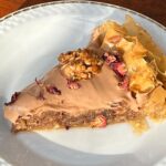 Maria Jekova Instagram - Спомени от отминали дни, преплетени с вкуса на настоящия живот. Какво значи за мен зима по мой вкус? По един начин свързвам зимата с празниците, каквато е и тази рецепта - отново извадена от дълбините на съзнанието ми, там, където са най-милите спомени. Направете празниците тази година по ваш вкус - както ще ви доставят радост на вас, сладост и спокойствие - пак на вас. Без суетене, без тревоги от очаквания. Като цяло това послание може да бъде извадено от контекста на зимата и да си пожелаем по-често да живеем по наш вкус. По-често, да не кажа - винаги. Това ще бъде и моето пожелание към вас, към тази новогодишна рецепта, която споделям с вас, вдъхновена от Jameson Black Barrel. Много хора си мислят, че обгарянето на бъчвите дава пиперлив аромат и вкус на уискито, а всъщност то задълбочава, подслажда и карамелизира вкусовете и уханията, като ги прави съвършени за съчетание с десерти, а и в такива. Ако това е моята зима, то Jameson Black Barrel те кани да създадеш зима по твой вкус, като тази година те раздават и награди, изрисувани от българския артист Борис Праматаров. Повече информация ще намерите на jbbwinter.com. А сега към рецептата на моята зима. Четири слоя фини точени кори се редят във форма за тарт, а между тях смлени орехи и масло. Два фитила с пълнеж от орехи се навиват и се засукват като обръч около ръба на формата - както съм показала във видеото - те ще задържат плънката в центъра. Изпича се за 5 минути, сякаш печем маслена основа за тарт. След това правим орехов кекс, който разстиламе в средата. Смесваме първо: 3 жълтъка, 50 грама кафява захар, 100 грама смлени орехи и 100 грама ръжено брашно, 10 грама бакпулвер, щипка сол и 50 мл Jameson Black Barrel. Разбиваме 3 белтъка на сняг и ги влагаме накрая. Печем за 10 минути на 180 градуса. Оставяме да изстине, като през това време правим сироп от 500 грама кафява захар, 3 резена лимон, 100 мл розова вода, 100 мл Jameson Black Barrel и 400 мл вода. Заливаме студената баклава с горещия сироп. Накрая правим крем от една кофичка заквасена сметана, 150 грама мармалад от шипки с петмез и 50 мл Jameson Black Barrel. Завършваме с карамелизирани орехи и сушени венчелистчета от цвят на шипка.