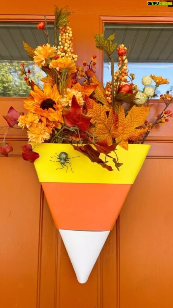 Meaghan B. Murphy Instagram - DIY candy corn 🌽 door hanger—don’t call it a wreath 🤣 HOW TO: ✂️ Cut a triangle out of foam ✂️ Cut yellow, orange & white strips out of craft foam paper. Tip: You can use tissue or construction paper if you’re hanging it indoors 🧵 Wrap the strips around the triangle and secure with sewing 🪡 pins 💐 Stick faux flowers in the top 🕷 Add a spider to make it truly spooktacular #wdcelebrates #wreathsofinstagram #wreathmaking #wreath #halloweendecor Halloween Headquarters