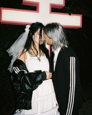 Nadezhda Tolokonnikova Instagram - 💍🔪🫀 american boy уеду с тобой

@voguemagazine 📝: Sewing used to be a source of trauma for Pussy Riot’s Nadya Tolokonnikova, who was forced to stitch military and police uniforms while in a Russian penal colony. 

But she decided to reclaim the activity when she sewed Adidas stripes onto her now-husband John Caldwell’s suit jacket, for their wedding on 12 January. “Now I feel like I can sew again without being necessarily connected to the traumatic experience,” she says. “It broke the chain of trauma.”

She wanted to create contrast between the “cute” side of her personality with the “gopnik” side. Tolokonnikova, who is vegan, juxtaposed her sweet look with an oversized black faux-leather Adidas jacket. She also wore a pair of velvet Doc Martens, though she changed into slides from—you guessed it—Adidas during the party. 

Tolokonnikova also included the Orthodox cross in her ceremony: on a necklace, garter belt, and even the vegan Napoleon cake covered in black icing, which she baked herself. “I’m almost trying to steal [the symbol] from the Orthodox Christianity, honestly, because they stole two years of my life,” she says. “I was accused—besides going against Putin—of religious hatred, which I didn’t have. But they still accused me of it. So I was like, Well, I’m just going to be using your symbol and reclaim it as my own.” She and Caldwell were married by Father Nathan Monk, who was excommunicated from the Russian Orthodox church for his support of the LGBTQ+ community, underneath a giant neon Orthodox cross. 

Photos: @marysergeevnaa 
Husbando: @vegsurfer 
Text: @hannahjacksuhn