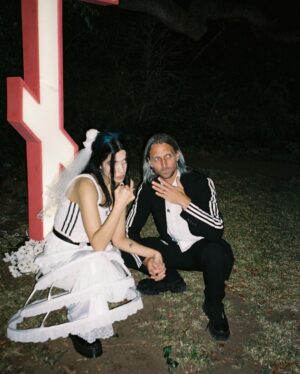 Nadezhda Tolokonnikova Instagram - 💍🔪🫀 american boy уеду с тобой

@voguemagazine 📝: Sewing used to be a source of trauma for Pussy Riot’s Nadya Tolokonnikova, who was forced to stitch military and police uniforms while in a Russian penal colony. 

But she decided to reclaim the activity when she sewed Adidas stripes onto her now-husband John Caldwell’s suit jacket, for their wedding on 12 January. “Now I feel like I can sew again without being necessarily connected to the traumatic experience,” she says. “It broke the chain of trauma.”

She wanted to create contrast between the “cute” side of her personality with the “gopnik” side. Tolokonnikova, who is vegan, juxtaposed her sweet look with an oversized black faux-leather Adidas jacket. She also wore a pair of velvet Doc Martens, though she changed into slides from—you guessed it—Adidas during the party. 

Tolokonnikova also included the Orthodox cross in her ceremony: on a necklace, garter belt, and even the vegan Napoleon cake covered in black icing, which she baked herself. “I’m almost trying to steal [the symbol] from the Orthodox Christianity, honestly, because they stole two years of my life,” she says. “I was accused—besides going against Putin—of religious hatred, which I didn’t have. But they still accused me of it. So I was like, Well, I’m just going to be using your symbol and reclaim it as my own.” She and Caldwell were married by Father Nathan Monk, who was excommunicated from the Russian Orthodox church for his support of the LGBTQ+ community, underneath a giant neon Orthodox cross. 

Photos: @marysergeevnaa 
Husbando: @vegsurfer 
Text: @hannahjacksuhn