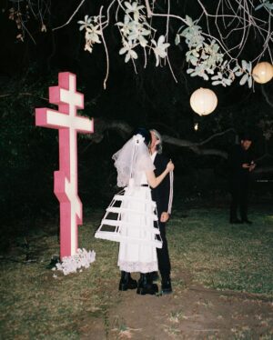 Nadezhda Tolokonnikova Instagram - 💍🔪🫀 american boy уеду с тобой

@voguemagazine 📝: Sewing used to be a source of trauma for Pussy Riot’s Nadya Tolokonnikova, who was forced to stitch military and police uniforms while in a Russian penal colony. 

But she decided to reclaim the activity when she sewed Adidas stripes onto her now-husband John Caldwell’s suit jacket, for their wedding on 12 January. “Now I feel like I can sew again without being necessarily connected to the traumatic experience,” she says. “It broke the chain of trauma.”

She wanted to create contrast between the “cute” side of her personality with the “gopnik” side. Tolokonnikova, who is vegan, juxtaposed her sweet look with an oversized black faux-leather Adidas jacket. She also wore a pair of velvet Doc Martens, though she changed into slides from—you guessed it—Adidas during the party. 

Tolokonnikova also included the Orthodox cross in her ceremony: on a necklace, garter belt, and even the vegan Napoleon cake covered in black icing, which she baked herself. “I’m almost trying to steal [the symbol] from the Orthodox Christianity, honestly, because they stole two years of my life,” she says. “I was accused—besides going against Putin—of religious hatred, which I didn’t have. But they still accused me of it. So I was like, Well, I’m just going to be using your symbol and reclaim it as my own.” She and Caldwell were married by Father Nathan Monk, who was excommunicated from the Russian Orthodox church for his support of the LGBTQ+ community, underneath a giant neon Orthodox cross. 

Photos: @marysergeevnaa 
Husbando: @vegsurfer 
Text: @hannahjacksuhn
