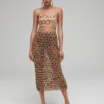 Natalia Fedner Instagram – Surprise!!! When @bloomingdales reached out to me about making a dress to celebrate the 50th anniversary of the Big Brown Bag – I was immediately on board! I wanted to bring my brand’s DNA to the project, while maintaining the integrity of the iconic Big Brown Bag kraft paper aesthetic. So I created a special chainmail made from actual Bloomingdale’s Big Brown Bags. This tiny paper chainmail, like my metal designs, is entirely hand made. The process starts by cutting the BBBs into 8.5 x 11” sheets, ironing them flat (yes, flashbacks to pressing paper patterns out at Parsons were had), then cutting the sheets into thousands of small strips using a hand held paper cutter (that I may have found tossed out on a street corner by my West Hollywood apartment…), and finally taping them together with little double sided tabs to create a honeycomb like pattern. I used this technique to create the skirt for the project, finishing it off with a Bloomingdales waistband (sourced from the side of the bag). The paper skirt is delicate, but because of the technique I developed for the project, it actually stretches quite a bit and allows a full range of movement! For the top, I wanted to design something a little more clean and simple that really focused on the theme. So I opted for a 90’s style bandeau top with the famous words front and center, integrating hand straps from actual bags to create shoulder straps for the top. By incorporating a few smart darts in the front and some corset work in the back, I was able to transition a Big Brown Bag into a Small Sleek Top. The overall silhouette of the look gives a wink to the 1950s, celebrating Bloomingdales lasting impact on fashion. Swipe through for a small taste of BTS – more to come! And yes model @lamekafox IS wearing a pair of our own chain earrings! 

Shoutout to @riowarner and @maya_adelle – this was a true labor of love that involved thousands of little movements – little cuts, little bits of tape – and these two rockstars made sure I got the project done in time by helping prep thousands of paper tabs for me. And thank you @p810km for being our fit model 🥰 Thank you @ela.ine.k @tatootsie for bringing me on!!