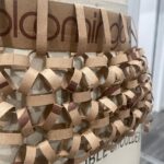 Natalia Fedner Instagram – Surprise!!! When @bloomingdales reached out to me about making a dress to celebrate the 50th anniversary of the Big Brown Bag – I was immediately on board! I wanted to bring my brand’s DNA to the project, while maintaining the integrity of the iconic Big Brown Bag kraft paper aesthetic. So I created a special chainmail made from actual Bloomingdale’s Big Brown Bags. This tiny paper chainmail, like my metal designs, is entirely hand made. The process starts by cutting the BBBs into 8.5 x 11” sheets, ironing them flat (yes, flashbacks to pressing paper patterns out at Parsons were had), then cutting the sheets into thousands of small strips using a hand held paper cutter (that I may have found tossed out on a street corner by my West Hollywood apartment…), and finally taping them together with little double sided tabs to create a honeycomb like pattern. I used this technique to create the skirt for the project, finishing it off with a Bloomingdales waistband (sourced from the side of the bag). The paper skirt is delicate, but because of the technique I developed for the project, it actually stretches quite a bit and allows a full range of movement! For the top, I wanted to design something a little more clean and simple that really focused on the theme. So I opted for a 90’s style bandeau top with the famous words front and center, integrating hand straps from actual bags to create shoulder straps for the top. By incorporating a few smart darts in the front and some corset work in the back, I was able to transition a Big Brown Bag into a Small Sleek Top. The overall silhouette of the look gives a wink to the 1950s, celebrating Bloomingdales lasting impact on fashion. Swipe through for a small taste of BTS – more to come! And yes model @lamekafox IS wearing a pair of our own chain earrings!
Shoutout to @riowarner and @maya_adelle – this was a true labor of love that involved thousands of little movements – little cuts, little bits of tape – and these two rockstars made sure I got the project done in time by helping prep thousands of paper tabs for me. And thank you @p810km for being our fit model 🥰 Thank you @ela.ine.k @tatootsie for bringing me on!!