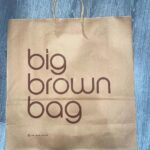 Natalia Fedner Instagram – Surprise!!! When @bloomingdales reached out to me about making a dress to celebrate the 50th anniversary of the Big Brown Bag – I was immediately on board! I wanted to bring my brand’s DNA to the project, while maintaining the integrity of the iconic Big Brown Bag kraft paper aesthetic. So I created a special chainmail made from actual Bloomingdale’s Big Brown Bags. This tiny paper chainmail, like my metal designs, is entirely hand made. The process starts by cutting the BBBs into 8.5 x 11” sheets, ironing them flat (yes, flashbacks to pressing paper patterns out at Parsons were had), then cutting the sheets into thousands of small strips using a hand held paper cutter (that I may have found tossed out on a street corner by my West Hollywood apartment…), and finally taping them together with little double sided tabs to create a honeycomb like pattern. I used this technique to create the skirt for the project, finishing it off with a Bloomingdales waistband (sourced from the side of the bag). The paper skirt is delicate, but because of the technique I developed for the project, it actually stretches quite a bit and allows a full range of movement! For the top, I wanted to design something a little more clean and simple that really focused on the theme. So I opted for a 90’s style bandeau top with the famous words front and center, integrating hand straps from actual bags to create shoulder straps for the top. By incorporating a few smart darts in the front and some corset work in the back, I was able to transition a Big Brown Bag into a Small Sleek Top. The overall silhouette of the look gives a wink to the 1950s, celebrating Bloomingdales lasting impact on fashion. Swipe through for a small taste of BTS – more to come! And yes model @lamekafox IS wearing a pair of our own chain earrings!
Shoutout to @riowarner and @maya_adelle – this was a true labor of love that involved thousands of little movements – little cuts, little bits of tape – and these two rockstars made sure I got the project done in time by helping prep thousands of paper tabs for me. And thank you @p810km for being our fit model 🥰 Thank you @ela.ine.k @tatootsie for bringing me on!!
