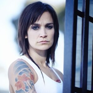 Nicole da Silva Instagram - What does this image of Franky have to do with #afghanistan🇦🇫 ? There’s news to come. In the meantime, head to the link in my bio to find out how you can help Afghan women and girls 💥 @unwomenaust 📸 @benkingphotographer 

Image Description: Nicole da Silva as Franky Doyle stands in front of prison bars with short cropped hair, rats tail and arm tattoo.