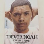 Pedro Ribeiro Instagram – Como é que se acaba de ler a biografia de um humorista, e se tem vontade de chorar?
O sul africano do Trevor Noah é um daqueles casos de alguém que contraria todas as probabilidades, e quem ler a sua história não pode deixar de pensar que aqui está um homem que é de facto uma improbabilidade. E no entanto, ei-lo a sair vivo e bem, do lado de cá, depois do inferno.
O retrato da África do Sul do Apartheid, com 11 línguas oficiais e infinitos outros dialetos, das várias camadas de crime e coragem que se cruzam, como se cruzam esperança e desalento, racismo e optimismo, fé e ausência absoluta de noção entre o bem e o mal, ingenuidade e esperteza, polícia criminosa e gangsters ingénuos, um sistema corrupto e uma economia paralela, violência doméstica e sentido de comunidade, tudo ao mesmo tempo, opostos absurdos que fizeram a infância e adolescência deste tipo que eu só conhecia do Daily Show e que agora me parece estranhamente próximo, mais real. O puto que deu a volta ao destino. E fê-lo com surpreendente sanidade suficiente para ser o autor da melhor, mais eloquente e fiel descrição do prazer único que é fazer cocó quando se tem mesmo vontade.
“Sou um Crime”, chama-se o livro.
Não o ler é que é, eu acho.