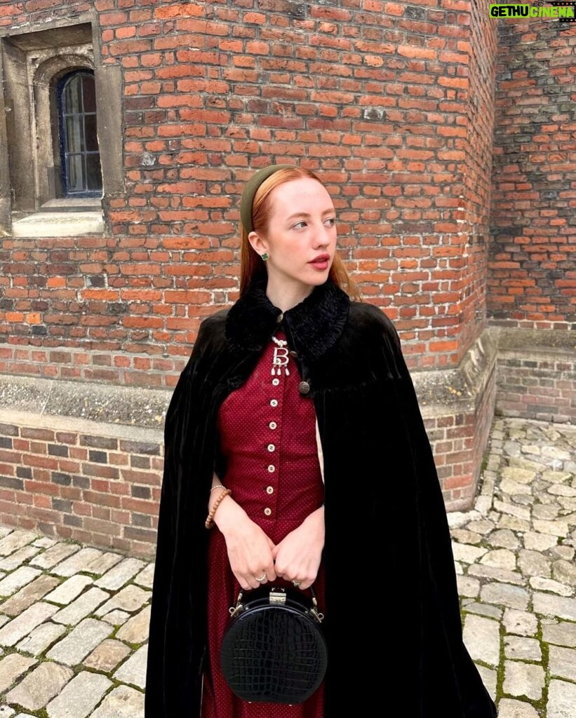 Rebecca Flint Instagram - if you can’t wear a cape in hampton court palace i’m not sure where you can 🌹? I have always wanted to see this incredible tudor palace for myself and I was so excited to have the chance! they had live cooking demonstrations inside the original kitchens, and we saw so many amazing tapestries and paintings… incredible day to visit! the puff headband trend always reminds me of the French Hood so I had to wear this army green one, along with this spectacular velvet and silk cape picked up from @classiccarbootsale in the spring! My dress is vintage from Japan, and my bag is @aspinaloflondon. The shoes are @empressaustralia 🔍 Not forgetting my B necklace as an homage to Anne 🅱️❤️ Hampton Court Palace