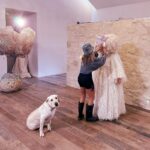 Sia Instagram - Coming soon #GimmeLove 👀 - Team Sia [image description: a woman styling Sia, who is in a white wig and dress, with a white dog sitting in front of them]