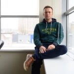 Alexey Navalny Instagram - Я - икона осознанного потребления. В моей камере есть только кружка и книга. Ложку и тарелку дают на время еды. И даже тюремную мою одежду забрали, выдав временную. Теперь на моей спине огромные белые буквы: ШИЗО. Всем привет из штрафного изолятора. Настоящая профсоюзная борьба никогда не бывает легкой, чего уж говорить о профсоюзе в тюрьме. Кремль хочет видеть свой ГУЛАГ состоящим из безмолвных рабов. А тут я вместо того, чтобы умолять о помиловании, кого-то объединяю и требую соблюдения каких-то законов. Поэтому меня вызвали из барака на комиссию, где объявили, что на видеозаписях видно: я, находясь на промзоне, регулярно расстегиваю верхнюю пуговицу робы. Это, безусловно, характеризует меня как неисправимого злодея. Поэтому принято решение водворить меня в штрафной изолятор. Пока на 3 суток, но - радостно улыбнулся и.о. начальника, - в середине сентября у меня свидание с родственниками. Содержащимся в ШИЗО свидания запрещены, поэтому если я “не пересмотрю свое отношение”, то изолятор станет моей постоянной резиденцией. Непонятно, отношение к чему я должен пересмотреть. К рабскому труду? К Путину? ШИЗО - самое суровое наказание в легальной тюремной иерархии. Впрочем, в нелегальной тоже - пытают и убивают чаще всего именно здесь. Устроено это так. Бетонная конура 2,5х3 метра. Чаще всего там невыносимо, потому что холодно и сыро. У меня пляжный вариант - очень жарко и почти нет воздуха. Форточка крохотная. Вентиляции нет. Ночью лежишь и чувствуешь себя рыбой на берегу. Железная койка пристегивается к стене. В 5 утра забирают матрас и подушку (это называется “мягкий инвентарь”) и поднимают койку. В 9 вечера койку снова опускают. Железный стол и лавка, раковина, дырка в полу. Под потолком две камеры. Свидания запрещены, письма запрещены, передачи запрещены. Единственное место в тюрьме, где даже курение запрещено. Бумагу и ручку дают на 1 час 15 минут в день. Прогулка - час в такой же камере, но с куском неба. Все время обыски и руки за спиной. Вот сижу сейчас на железной лавке за железным столом. Допишу этот пост и буду писать инструкцию для зэков об их правах на рабочем месте, пока не заберут бумагу. Права комиссия: кажется, я неисправим 😉