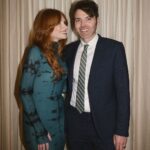 Bryce Dallas Howard Instagram – Today is 23 years since we started dating, and each day gets better and better. I love you handsome.⁣
⁣
📸: @andiejjane 
⁣
[ID: Dressed up for a night out, BDH (left; wearing her hair down and a fitted dress with a moss & black dye print) and Seth Gabel (right; wearing a navy blue suit, white button-down shirt, and a gray and yellow tie) take a photo together in front of a tan curtain. BDH smiles softly at Seth.]