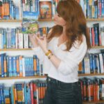 Bryce Dallas Howard Instagram - Returning to the motherland this week #Ireland 🇮🇪⁣⁣ ⁣⁣ 📸: @andiejjane⁣⁣ ⁣⁣ [ID: Wearing a white blouse and blue jeans, BDH stands in front of a bookcase with shelves and shelves of miscellaneous travel guides. She holds the Lonely Planet guide for Ireland by her face, absolutely ecstatic about returning to Ireland after 30 years!!]