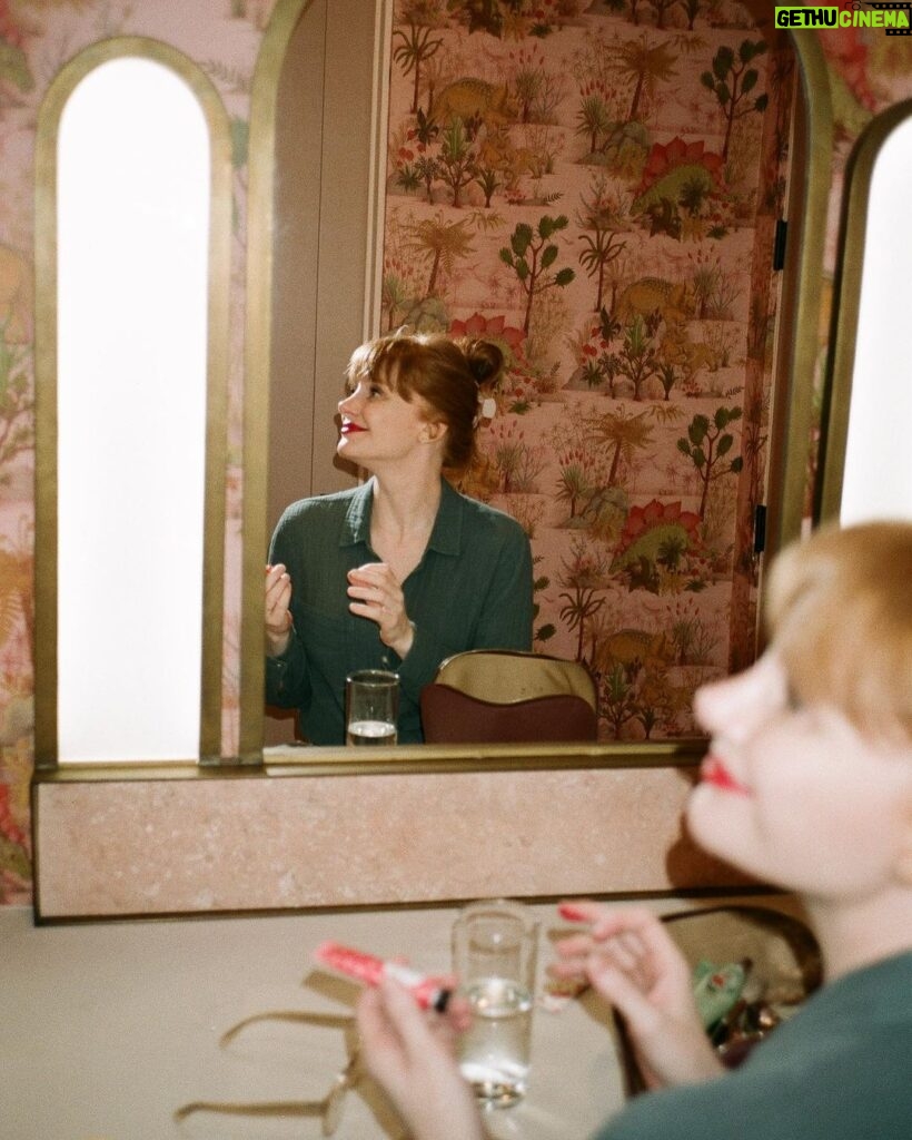 Bryce Dallas Howard Instagram - 💋💋💋⁣⁣⁣ ⁣ 📸: @andiejjane ⁣⁣⁣ [ID: In blue jeans and a teal linen blouse, BDH sits on her vanity by the mirror. She wears her hair up in a clipped bun and applies Bakeup Beauty’s neutral palm eyeshadow palette and Yolaine’s red lip.]