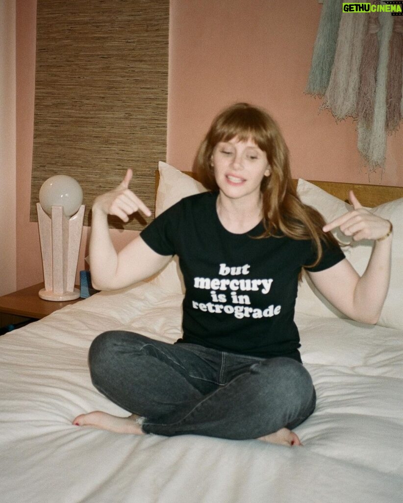 Bryce Dallas Howard Instagram - Mercury is Retrograde! In Virgo! To use the words of astrologer and writer @chaninicholas, “Good luck to us all!”⁣⁣ ⁣ 📸: Andie Jane (@andiejjane)⁣⁣ ⁣⁣ [ID: BDH sits cross-legged on top of a fluffy white comforter. She points to her black t-shirt which reads, “but mercury is in retrograde.”]