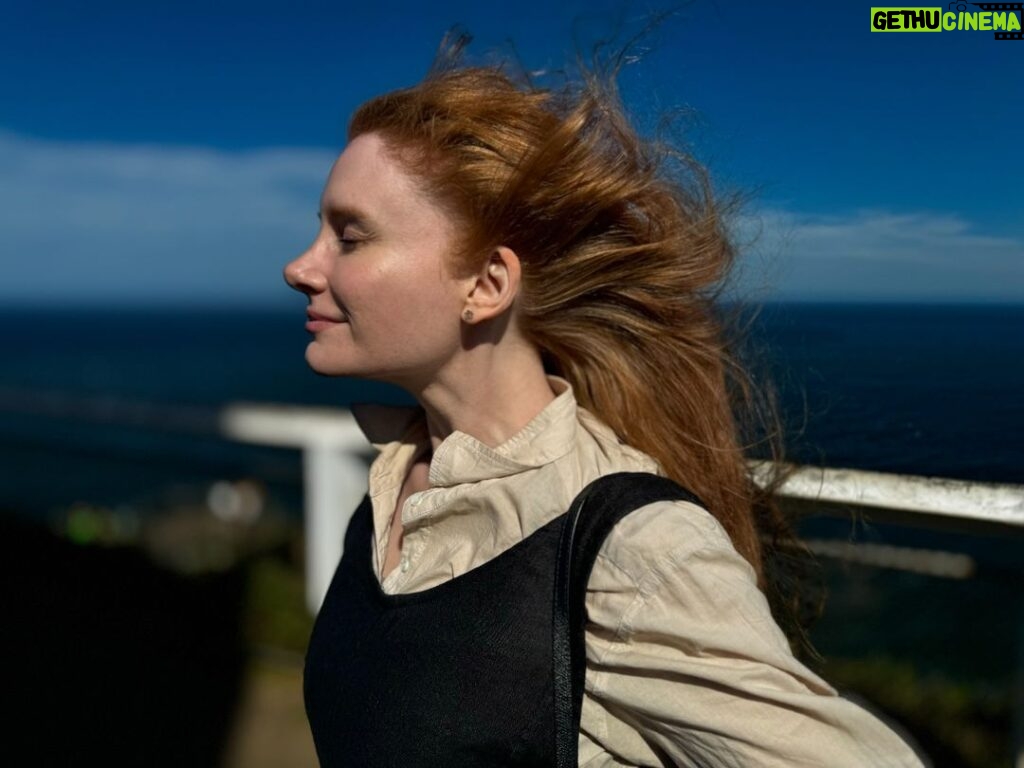Bryce Dallas Howard Instagram - Going into 2024 like... [ID: In a close-up profile, BDH stands with her eyes closed as the Australian summer breeze sweeps her hair back. She dresses in cream and navy linen and a slight smile grows on her face. In the background, the bright blue waters of Byron Bay.]