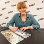 Bryce Dallas Howard Instagram - 8 hours of signatures later 😅 It means the world that fans across the movie multiverses want to memorialize these stories!! Thank you @swau_official for organizing such a fantastic signing day — my inner fangirl had the time of her life⁣ ⁣ and p.s. @missmistyrosas, @chrisfbartlett, @therealbrendanwayne, and @lateefcrowderdossantos: it’s always an honor to put my signature next to yours ❤️⁣ ⁣ [ID: BDH, wearing a linen teal button down blouse, smiles as she signs a Claire Dearing / Jurassic World poster]