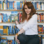 Bryce Dallas Howard Instagram - Returning to the motherland this week #Ireland 🇮🇪⁣⁣ ⁣⁣ 📸: @andiejjane⁣⁣ ⁣⁣ [ID: Wearing a white blouse and blue jeans, BDH stands in front of a bookcase with shelves and shelves of miscellaneous travel guides. She holds the Lonely Planet guide for Ireland by her face, absolutely ecstatic about returning to Ireland after 30 years!!]