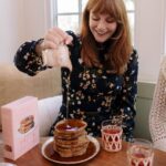 Bryce Dallas Howard Instagram - “Keep pouring,” they said 🤣 Upgrading my Sunday brunch game with @sweetlaurelbakery’s simple and delicious pancake mix 💕 Gluten-free, dairy-free, and paleo, there’s no going wrong here — place your order today at Sweet Laurel’s website in my bio:)⁣ ⁣ (not an ad, just a MASSIVE fan!)⁣ ⁣ [ID: BDH is living out her breakfast dreams as she pours a pitcher of syrup over a stack of Sweet Laurel pancakes. Smiling, she wears a navy dress with a peach and white floral pattern.]