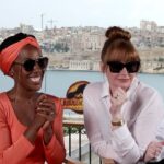 Bryce Dallas Howard Instagram - Going into the week like…⁣ ⁣ [ID: While in Malta for press, DeWanda Wise wears an apricot dress & BDH wears a white linen shirt. They make expressions that match their personalities to a tee: DeWanda smiles gleefully and Bryce leans toward her conspiratorially with a smirk. They sit in black directors chairs and behind them is the beautiful Maltese shoreline.]