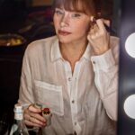 Bryce Dallas Howard Instagram - Getting ready for the last day of #JurassicWorldDominion press 🥹 Thank you @alanomiller for capturing this moment ❤️⁣ ⁣ [ID: A candid photo of BDH applying blush in front of a vanity mirror. She wears a flowy white Everlane button-down shirt and Apple Doll lipstick]