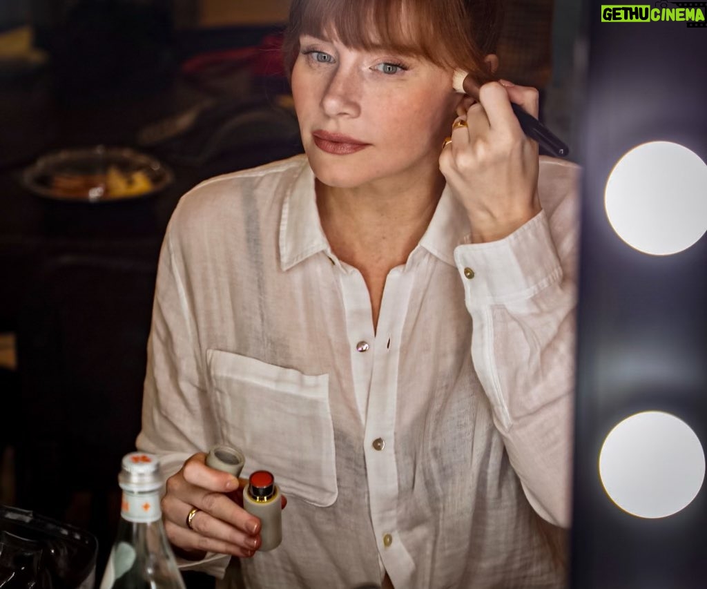 Bryce Dallas Howard Instagram - Getting ready for the last day of #JurassicWorldDominion press 🥹 Thank you @alanomiller for capturing this moment ❤️⁣ ⁣ [ID: A candid photo of BDH applying blush in front of a vanity mirror. She wears a flowy white Everlane button-down shirt and Apple Doll lipstick]