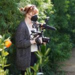 Bryce Dallas Howard Instagram – They say a director must become one with their environment 😉🌳 I’m filming my second documentary feature for @disneyplus and am very excited for you see what’s on the other side of the camera! ⁣
⁣
For all the film techies out there, this is @canonusa’s EOS C300 — I was so lucky to be one of the first directors to test this camera back in 2011 for my short film “When You Find Me” 🚀 I absolutely love how intuitive it is to operate. 100% recommended. ⁣
⁣
[ID: BDH in a grey cardigan, white v-neck, and black leggings becoming one with tall hedges, holding a Canon camera. 📸: @fullyjacked]