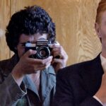David Bowie Instagram - Not much evidence of a mirror in this first shot from 1975 of Bowie as Thomas Jerome Newton, until you look at those famous eyes. All is revealed in the uncropped image as Geoff MacCormack is seen taking the shot in David’s changing room on the set of The Man Who Fell To Earth. Have you read Geoff’s book DAVID BOWIE: ROCK 'N' ROLL WITH ME? It’s a touching account of a lifelong friendship, peppered with Geoff’s extraordinary shots of David at work, rest and play: https://bit.ly/RockNRollWithMeBook (Linktree in bio) #BowieReflections