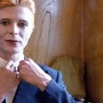David Bowie Instagram - Not much evidence of a mirror in this first shot from 1975 of Bowie as Thomas Jerome Newton, until you look at those famous eyes. All is revealed in the uncropped image as Geoff MacCormack is seen taking the shot in David’s changing room on the set of The Man Who Fell To Earth. Have you read Geoff’s book DAVID BOWIE: ROCK 'N' ROLL WITH ME? It’s a touching account of a lifelong friendship, peppered with Geoff’s extraordinary shots of David at work, rest and play: https://bit.ly/RockNRollWithMeBook (Linktree in bio) #BowieReflections