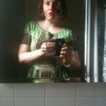 Lena Dunham Instagram – Recently I came across this photo of me at 24. I could remember exactly where I was when it was taken- the bathroom of a bar in the dead heat of August, wearing a vintage dress of my mother’s, with this overwhelming feeling (the kind you only get when you’re young) that you’re on the precipice of some big change. It got me dreaming about what that girl would have thought if I could appear in that mirror and tell her what the next 10 years would hold. “Hello, it’s me, 34 year old Lena. You’re not gonna believe this but in, like, 2 months you’re going to start on six seasons of a TV show. Are people gonna like it? That’s a… complex question, but you will love making it, and you will learn exactly what your own voice sounds like. Oh, and you’re going to write books. Like, WHOLE books. And yes, you will fully move out of your parents house and all the way to freakin’ California- don’t worry, I know it’s Hollywood but you won’t have to lose weight, in fact you’ll gain it- and sometimes even to the UK. And yes, you have a million friends and collaborators you love and you aren’t lonely in the ways you are now. Which is good because yeah, you know those random stomach aches? There’s, like, a bunch of surgery coming. They’re going to take out your uterus, which I know sounds kinda random but trust me, it’s a bigger deal once you’re older. And then you’ll have to get sober. But you don’t have a drug problem? Oh, please hold for that. And by the time you’re my age you’ll have kissed approximately 47 men (you still keep a list!) and literally none of them will be your husband. And you STILL can’t fucking drive. But you know the weird part? It’s all okay. It’s better than okay. It’s exactly what you were hoping for when you went into the bathroom and held this brand new thing called an iPhone up to the mirror thinking ‘something great is coming.'”