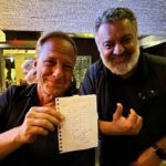 Mike Rowe Instagram - I was in Scottsdale yesterday, replenishing my electrolytes at a bar when a man introduced himself. “My name is Sy, and you probably won’t remember this, but we met on the streets of SF in 2007.” “Of course,” I said. “I’ll never forget that day.” Sy laughed. “You were kind of a smart aleck back then, too.” “I guess some things never change,” I said. With that, Sy opened a small notebook and removed a piece of folded looseleaf from the inside flap. “Here,” he said. I looked at the paper and recognized my signature, along with my trenchant bon mot, and wondered why this man would carry it around for 17 years. “I have no idea why I asked for your autograph in the first place. I mean, I liked Dirty Jobs, but I’ve never asked anyone for their signature before, or since. Isn’t that strange?” I nodded and agreed. It did seem strange, but not nearly as strange as what happened next. The bartender, a tall guy named Kenny asked me if I’d care for another. “Sure, and whatever Sy here is having.” When Kenny returned with our drinks he said, “You probably won’t remember this Mike, but we met back 2007.” “Did you say 2007?” “Yep.” I looked at Sy and said, “Do you guys know each other?” Both men shook their heads. Kenny continued. “You were in a bar on Mackinac Island. You guys were having a big night.” I asked, “Were you a bartender back there?” “No, I was just a guy who grew up watching Dirty Jobs.” “That’s quite a coincidence. Two guys in a random bar, both of whom met me 17 years ago. I wish you’d taken a picture.” “Why is that?” asked Kenny. “Because it would be statistically impossible if both of you had evidence of our meeting.” “Not quite impossible,” said Kenny. With that, he pulled out his phone and started scrolling. 30 seconds later the evidence was downloaded from the cloud. “There we are,” said Kenny. “That’s me crouched down in front of everyone. And that’s you, in the plaid shirt drinking a beer.” It’s moments like these that make me wonder about the belief held by so many that everything happens for a reason. Personally, I’m still a guy who believes in coincidence…but not as much as I did before Sy and Kenny brought the receipts.
