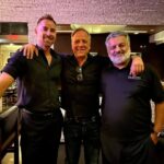 Mike Rowe Instagram - I was in Scottsdale yesterday, replenishing my electrolytes at a bar when a man introduced himself. “My name is Sy, and you probably won’t remember this, but we met on the streets of SF in 2007.” “Of course,” I said. “I’ll never forget that day.” Sy laughed. “You were kind of a smart aleck back then, too.” “I guess some things never change,” I said. With that, Sy opened a small notebook and removed a piece of folded looseleaf from the inside flap. “Here,” he said. I looked at the paper and recognized my signature, along with my trenchant bon mot, and wondered why this man would carry it around for 17 years. “I have no idea why I asked for your autograph in the first place. I mean, I liked Dirty Jobs, but I’ve never asked anyone for their signature before, or since. Isn’t that strange?” I nodded and agreed. It did seem strange, but not nearly as strange as what happened next. The bartender, a tall guy named Kenny asked me if I’d care for another. “Sure, and whatever Sy here is having.” When Kenny returned with our drinks he said, “You probably won’t remember this Mike, but we met back 2007.” “Did you say 2007?” “Yep.” I looked at Sy and said, “Do you guys know each other?” Both men shook their heads. Kenny continued. “You were in a bar on Mackinac Island. You guys were having a big night.” I asked, “Were you a bartender back there?” “No, I was just a guy who grew up watching Dirty Jobs.” “That’s quite a coincidence. Two guys in a random bar, both of whom met me 17 years ago. I wish you’d taken a picture.” “Why is that?” asked Kenny. “Because it would be statistically impossible if both of you had evidence of our meeting.” “Not quite impossible,” said Kenny. With that, he pulled out his phone and started scrolling. 30 seconds later the evidence was downloaded from the cloud. “There we are,” said Kenny. “That’s me crouched down in front of everyone. And that’s you, in the plaid shirt drinking a beer.” It’s moments like these that make me wonder about the belief held by so many that everything happens for a reason. Personally, I’m still a guy who believes in coincidence…but not as much as I did before Sy and Kenny brought the receipts.