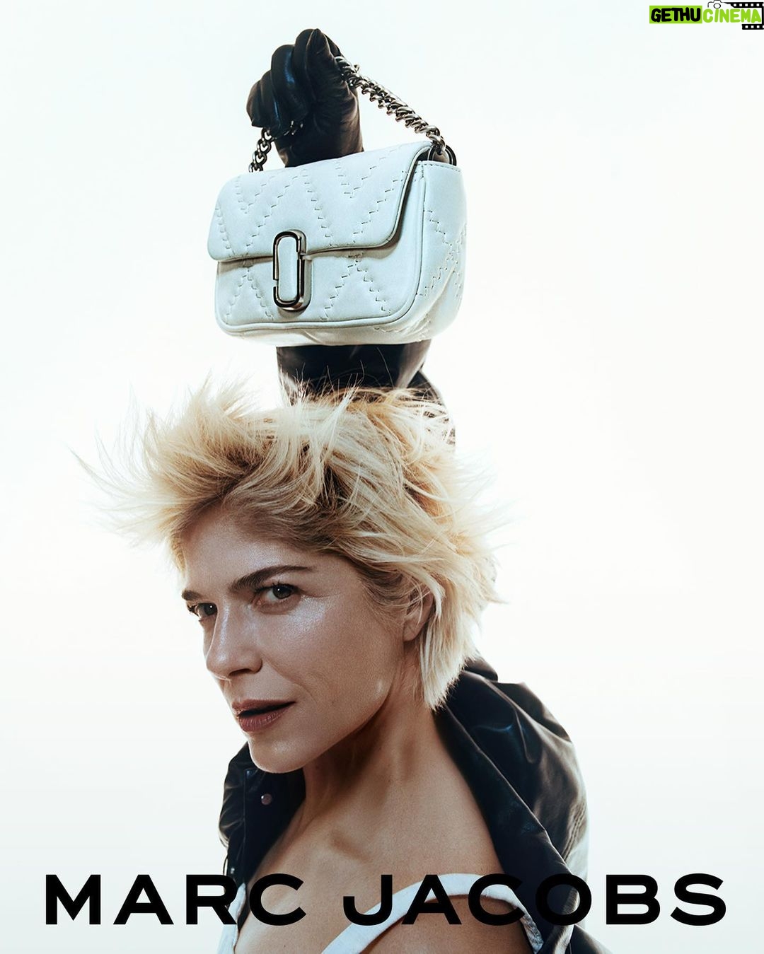 Selma Blair Instagram - It’s good to be back with the gang. Always love @marcjacobs. And our Stams. Image 1: Selma with short blonde hair, wearing all white clothes with white platform shoes, bends forward and holds a pink quilted bag. She is looking at the camera. Black text across the photo reads Marc Jacobs. Image 2: Selma with short blonde hair, wearing a black jacket, looks directly to the camera while holding a white bag over her head. Black text across the photo reads Marc Jacobs.