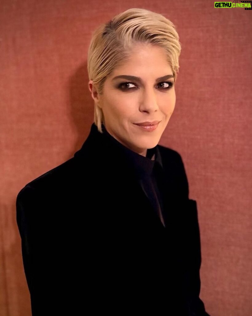 Selma Blair Instagram - The evening of Burberry. 🗡️ Image Descriptions: Image one: Selma has short blonde hair and wears a long black velvet coat. She is standing on the runway at the Burberry show with her cane with one hand in her pocket. Image two: Selma stands in front of orange wall. Image three: Selma sits with Edward and Naomi. Edward is wearing all black and Naomi is wearing a grey suit. Image four: Selma and Georgia are standing and both wearing black. Image five: Selma is standing in profile wearing a white robe while getting her hair done. Image six: Selma leans against an orange wall and is looking to the left.