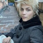 Selma Blair Instagram - 🤍🗽 Image Descriptions: 1. Selma has short blonde hair and is sitting on brick balcony wearing a grey coat with black collar. 2. Black/white photo of Selma and Christian Siriano at dinner. Christian has short dark hair and is wearing a black tshirt. 3. Selma is wearing a black sweater and sunglasses. A man is seated behind her playing with her dog Scout. 4. Black/white photo of Selma, Art Tavee and Carolyn Griffin at dinner. Art has short light hair and wears glasses and Carolyn has shoulder length hair. 5. Selma, Troy, Art, and Carolyn posing together for a selfie outside at dinner. 6. Selma posing in the mirror in a hotel bathroom. There are pink flowers in the focus of the photo. She wears a black sweater with a white collared shirt under it. New York, New York