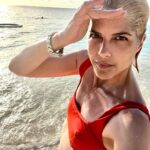 Selma Blair Instagram - It is a gift 🌊 Image description: Selma is standing on the beach with the sun and ocean behind her. She is wearing on orange bikini top and looking at the camera.